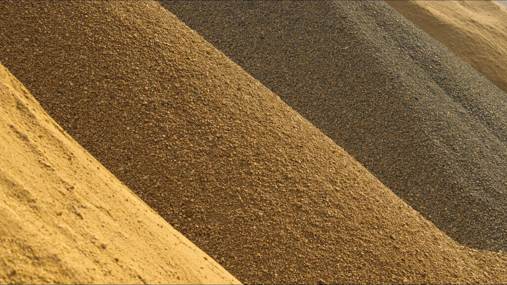 Drei Haufen aus Sand, Kies und Schotter in der Morgensonne